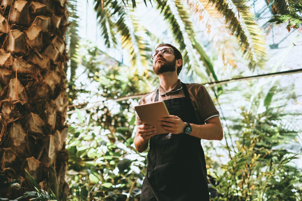 Young man gardener in glasses and apron with digital tablet working in a garden center